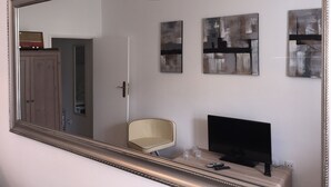Una habitación con un espejo grande, televisión, una silla y arte abstracto en la pared.