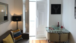 Una sala de estar moderna con un sofá, una mesa de comedor con tapa de vidrio y una puerta que da a otra habitación.