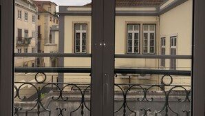 Un balcón con barandilla de hierro forjado que da a una hilera de edificios con numerosas ventanas, algunas con letras y números visibles.