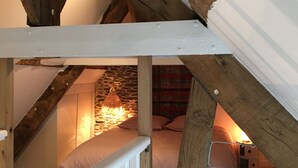 Een slaapkamer in een loft met zichtbare houten balken, een stenen muur en een hanglamp.