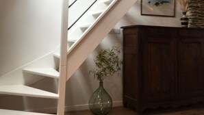 Een trap met witte leuning en houten treden, een vaas met plant en een houten kast.