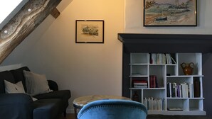 Een gezellige woonkamer met een open haard, een boekenkast en een schilderij van een kustlandschap.
