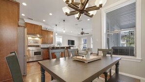 A modern kitchen with wooden cabinets, stainless steel appliances, and a dining area with a wooden table and chairs. - Beach Daze New 5BR, 4BA, 16 guest, Game Room. (Destin)