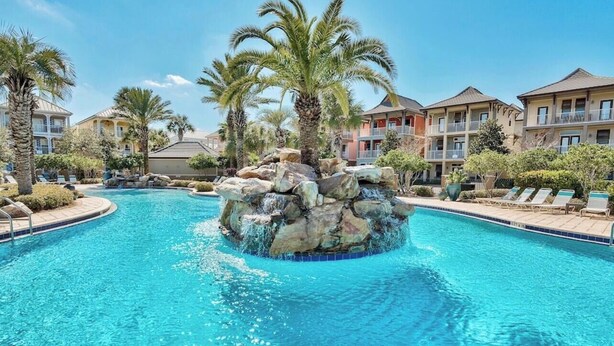 A swimming pool with a rock feature and palm trees, surrounded by multi-story buildings. - Beach Daze New 5BR, 4BA, 16 guest, Game Room. (Destin)