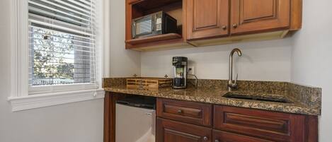 A kitchen with wooden cabinets, a built-in microwave, a coffee maker, and a dishwasher.