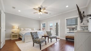 A bedroom with a bed, two patterned chairs, a white rug, a ceiling fan, and a large window with blinds. - Beach Daze New 5BR, 4BA, 16 guest, Game Room. (Destin)