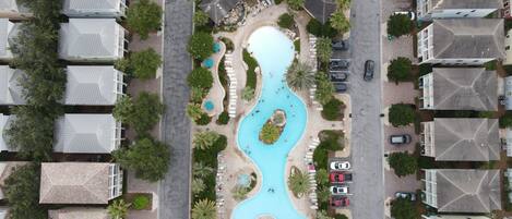 An aerial view of a residential area with a swimming pool, multiple cars, and houses with distinct roof designs.