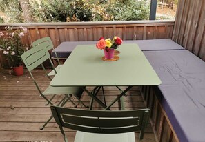 Une table en métal vert avec un coussin, une chaise et un vase rempli de fleurs, le tout posé sur une terrasse en bois.