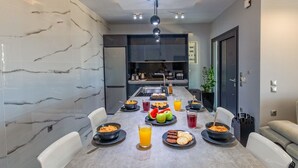 A modern kitchen with a marble backsplash, a dining table set with plates, bowls, and glasses, and a visible refrigerator. - AVITHOS BLUE VILLA  (kefalonia)