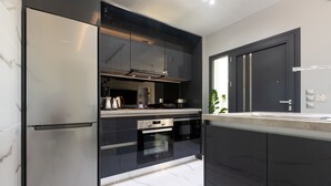 A modern kitchen with stainless steel appliances, black cabinetry, and a marble backsplash. - AVITHOS BLUE VILLA  (kefalonia)