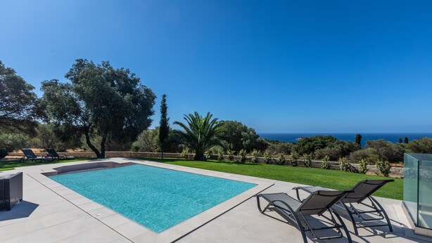 A swimming pool with lounge chairs and a table with fruit and drinks, surrounded by greenery and a view of the sea. - AVITHOS BLUE VILLA  (kefalonia)