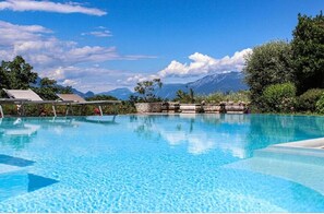 A clear blue pool with a mountain backdrop, surrounded by lush greenery and a stone structure. - Appartamento in Villa Elena (Lombardia)