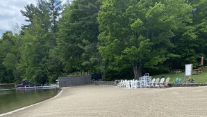 Ein Kiesstrand mit einer Anlegestelle und Booten, umgeben von Bäumen und einem weißen Zaun mit Stühlen.