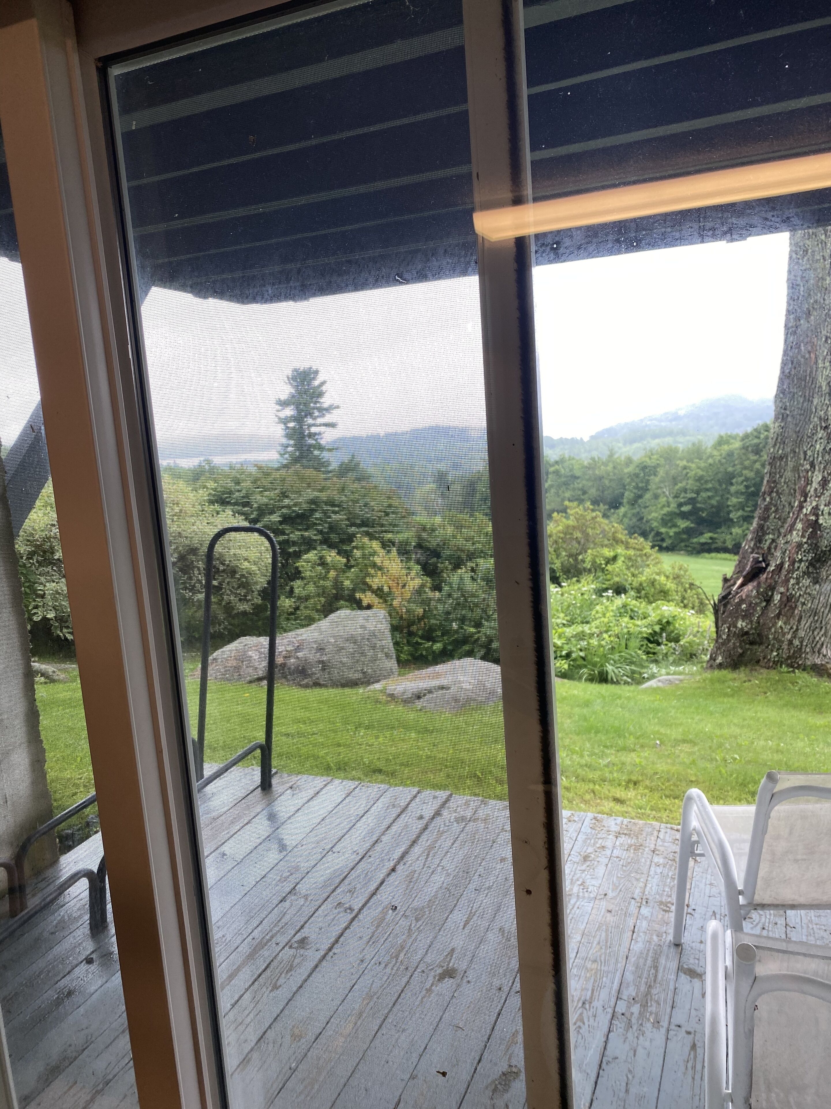 Vista desde una habitación con un ventanal grande que da a una zona verde con rocas y árboles.