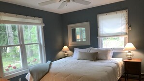 Ein Schlafzimmer mit einem großen Bett, zwei Nachttischen mit Lampen, einem Deckenventilator und Fenstern mit Vorhängen.