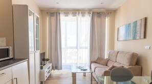 Un espacio habitable compacto con kitchenette, un sofá, una mesita de vidrio y un cuadro en la pared.