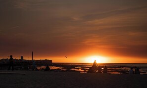 Escena de playa con gente y un atardecer.