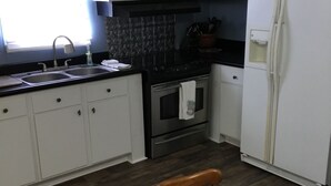A kitchen with white cabinets, a black countertop, a stainless steel stove, and a refrigerator. - Country living lake style near Santee  (Summerton)