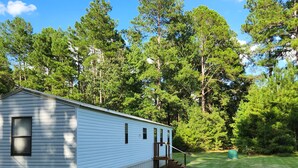 A single-story mobile home with a covered porch and a small deck, surrounded by a well-maintained lawn and tall trees. - Country living lake style near Santee  (Summerton)