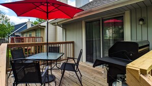 En terrasse med et bord, stole, en rød parasol og en grill.