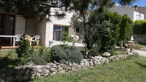 A house with a stone wall, a patio with chairs, and a garden with various plants. - Appartement T2 40 M² dans villa avec jardin Semaine /WE 2 personnes (Marseille)