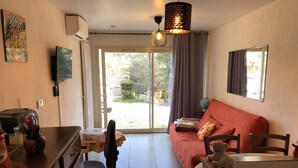 A compact living space with a sofa, a desk, and a chair. There is a globe on the desk and a window with curtains. - Appartement T2 40 M² dans villa avec jardin Semaine /WE 2 personnes (Marseille)
