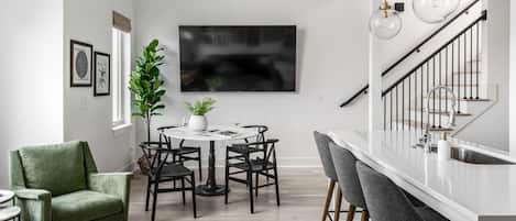 Una cocina moderna con encimera blanca, sillas negras y una mesa de comedor.