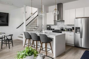 A modern kitchen with a central island, stainless steel appliances, and a staircase leading to an upper level. - Casa Paradisa • Rooftop, Fire Pit, Skyline Views (Nashville)