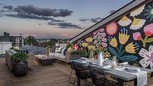 A rooftop terrace with a dining area, outdoor seating, and a colorful floral mural. - Casa Paradisa • Rooftop, Fire Pit, Skyline Views (Nashville)