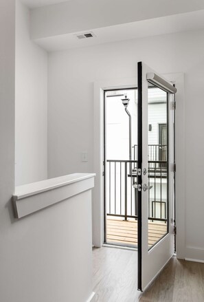 A hallway with a white door leading to a balcony with a wooden deck.