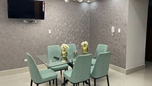 A modern dining area with a glass table surrounded by teal chairs, a mounted flat-screen TV, and a contemporary chandelier. - LUXURY EN EL MONUMENTO DE SANTIAGO DE LOS CABALLEROS (Santiago De Los Caballeros)