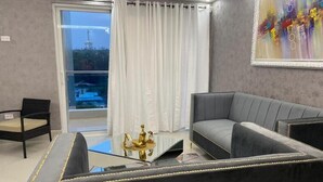 A modern living room with a grey sofa, a glass coffee table, and a view of a cityscape through a large window. - LUXURY EN EL MONUMENTO DE SANTIAGO DE LOS CABALLEROS (Santiago De Los Caballeros)