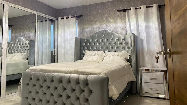 A bedroom with a tufted headboard, a bedside table, a mirror, and a wardrobe. - LUXURY EN EL MONUMENTO DE SANTIAGO DE LOS CABALLEROS (Santiago De Los Caballeros)