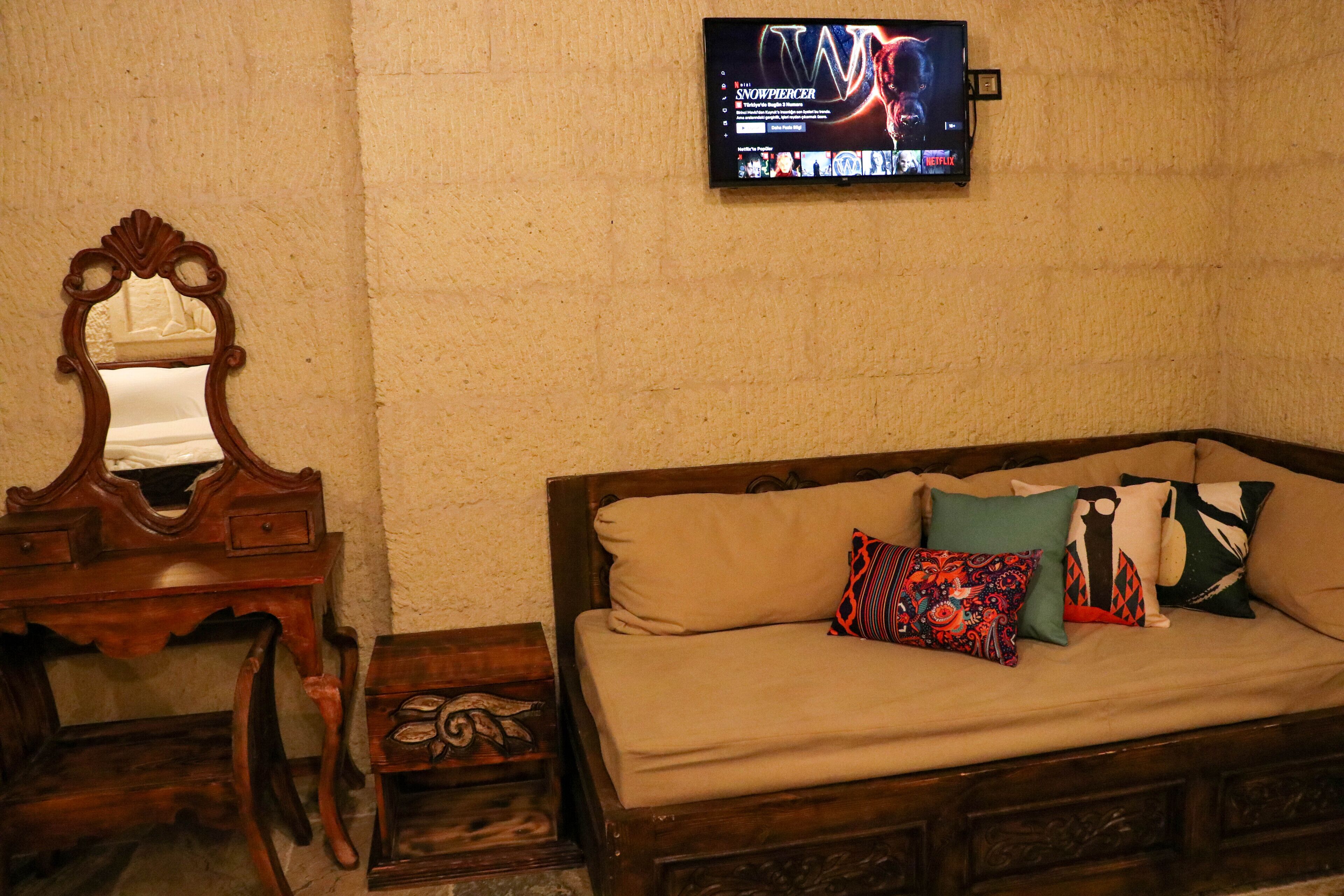 A room with a wooden bed, a wooden dresser, a mirror, and a television mounted on the wall.