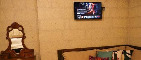 A room with a wooden bed, a wooden dresser, a mirror, and a television mounted on the wall.
