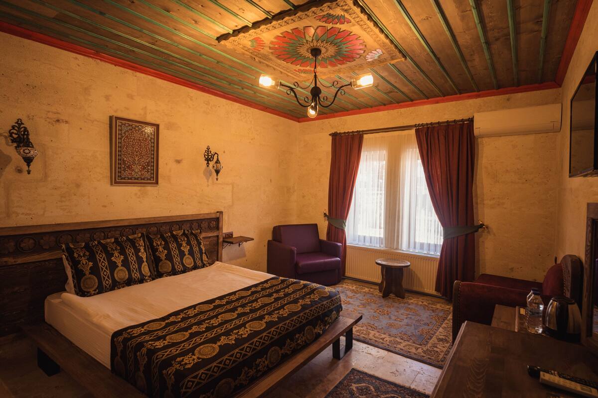 A traditional room with a bed, a chair, a small table, and a decorative ceiling.