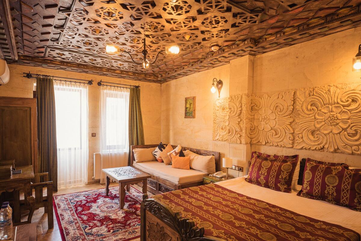 A room with a bed, a sofa, a table, and a chair. There is a patterned rug on the floor.