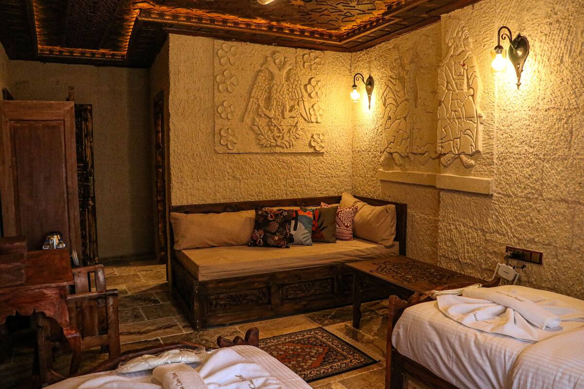 A cozy room with a wooden bench, a bed, and a stone wall with carvings. There are two wall-mounted lights and a wooden cabinet.