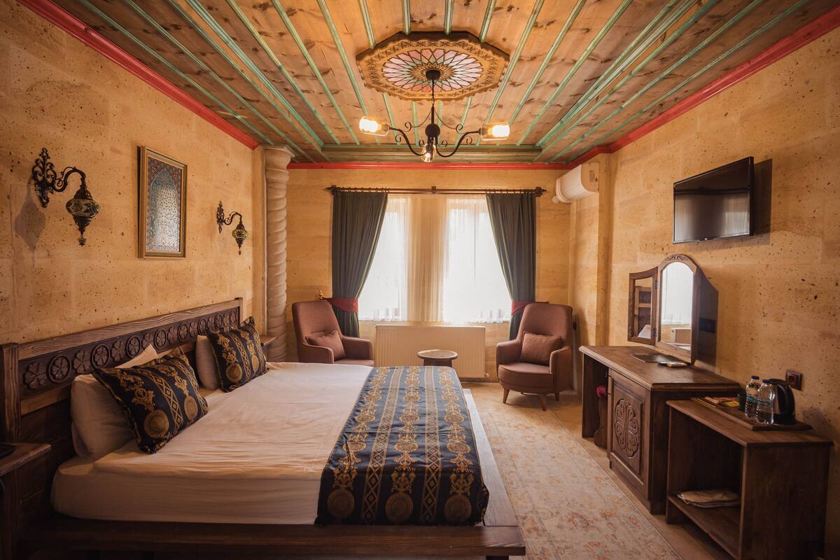 A hotel room with a large bed, two armchairs, a small table, a mirror, and a television.