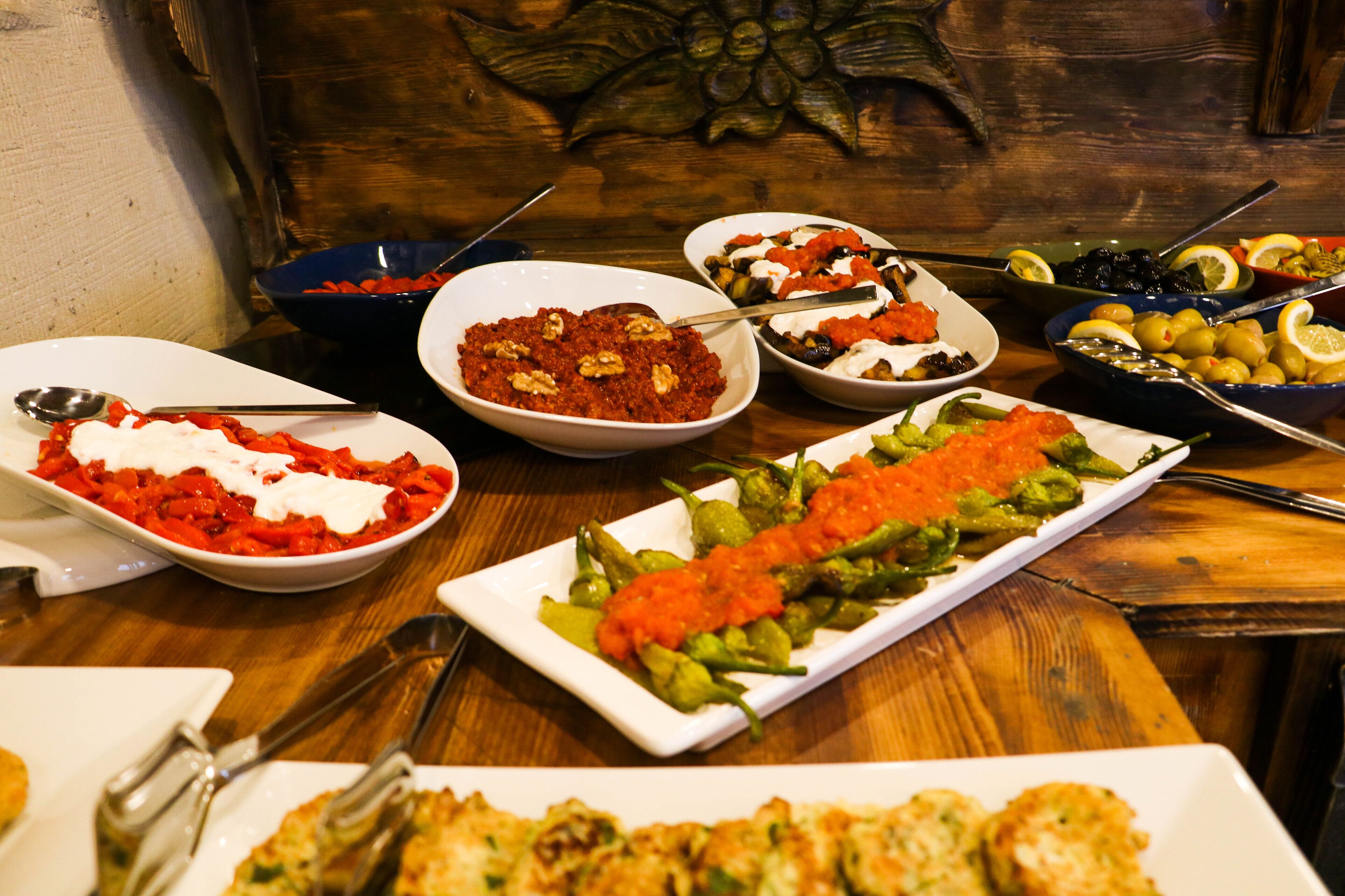 A variety of dishes on a wooden table, including salads, vegetables, and a dish with red sauce and nuts.
