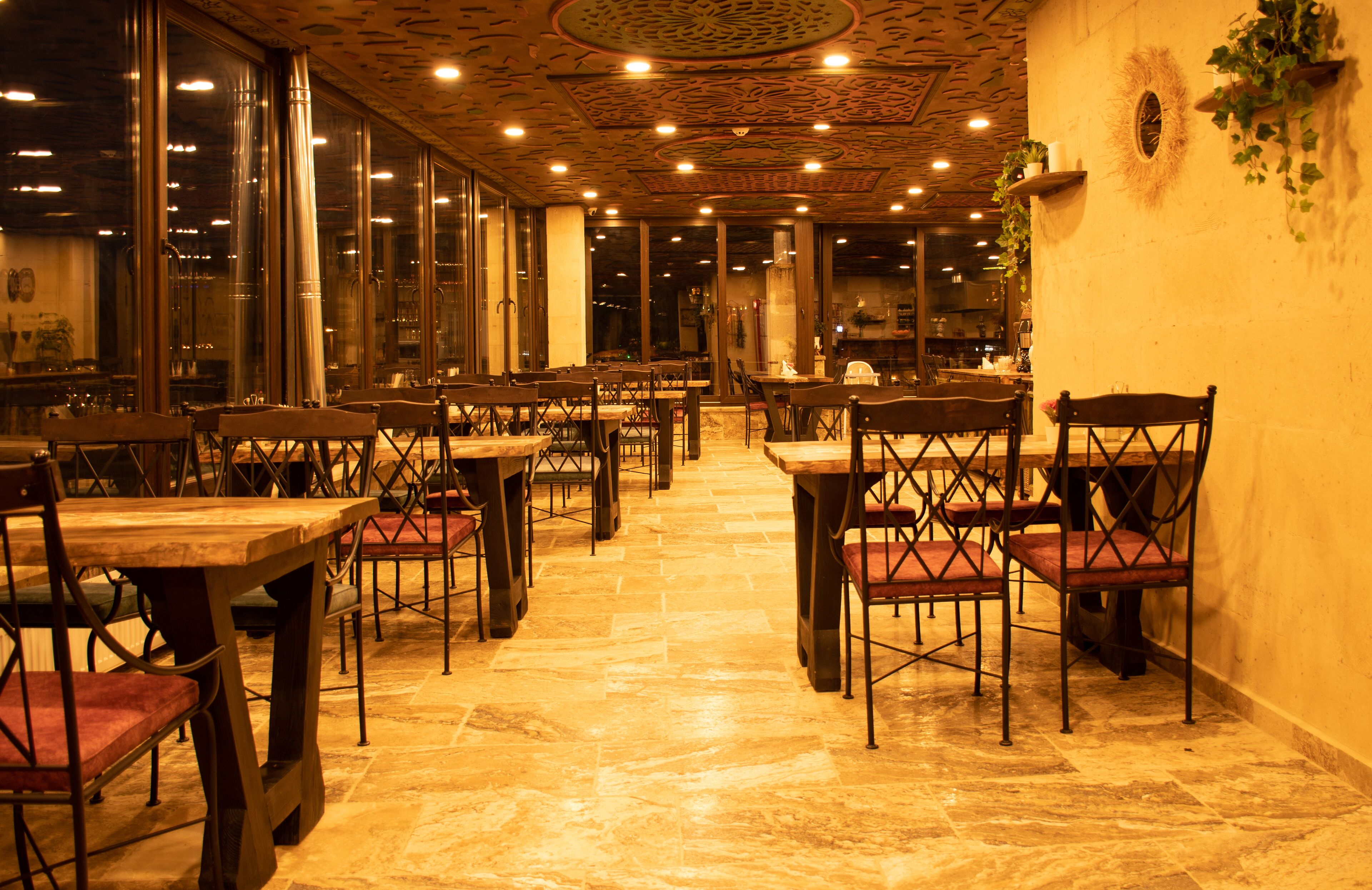 A restaurant with multiple tables and chairs, large windows, and a patterned ceiling.