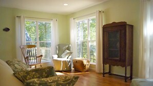 A cozy room with a wooden floor, a white sofa with patterned cushions, a rocking chair, and a wooden cabinet. - Scout's Hideaway on Beautiful Smith Lake (Arley)