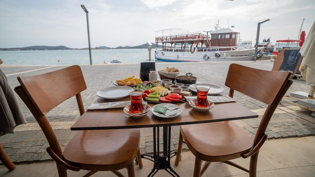 A table set for two with a view of the sea and a boat in the background. - Mai Otel Cunda (Ayvalik)