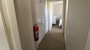 A hallway with a fire extinguisher mounted on the wall, leading to a bedroom with a bed and a nightstand. - Mai Otel Cunda (Ayvalik)