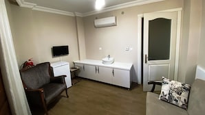 A compact living space with a kitchenette, a flat-screen TV, a sofa, and a patterned cushion. - Mai Otel Cunda (Ayvalik)