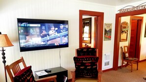 A hotel room with a television displaying a sports game, a wooden desk with a chair, and a door leading to another room. - River House on the McKenzie  (Rainbow)