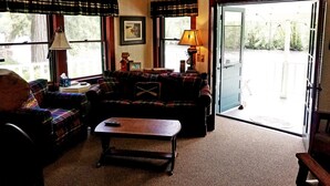 A cozy living room with a sofa, a coffee table, and a lamp. There is a door leading outside. - River House on the McKenzie  (Rainbow)