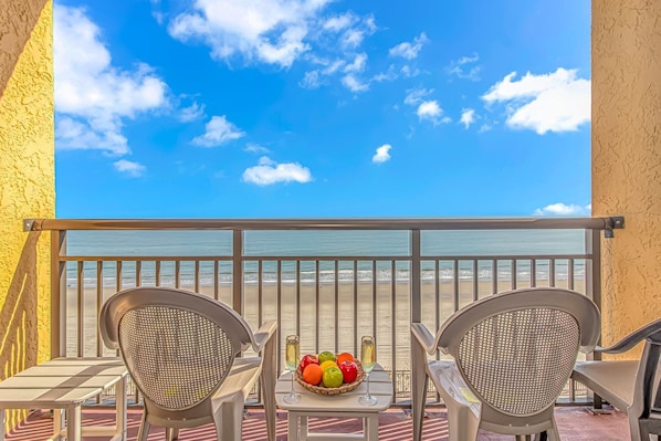 A balcony with two chairs, a table, and a fruit basket with a glass of wine.