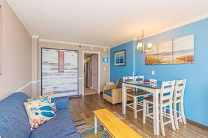 A living room with a sofa, a dining table with chairs, a bench, and a hallway leading to another room.