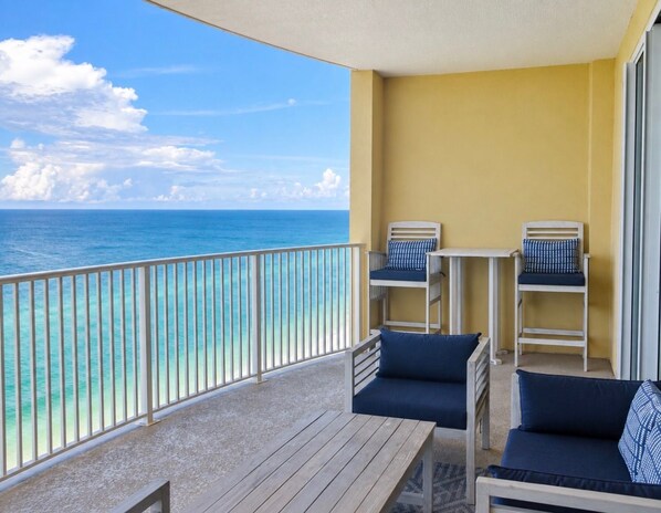 A balcony with a view of the ocean, two chairs, and a small table.